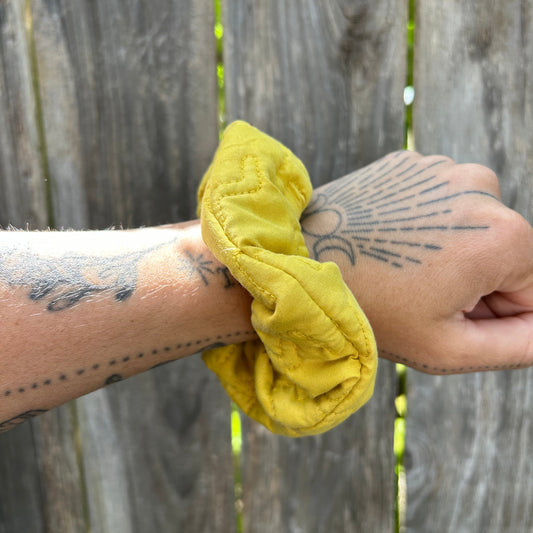 Yellow scrunchie on a wrist with tattoos against a wooden background