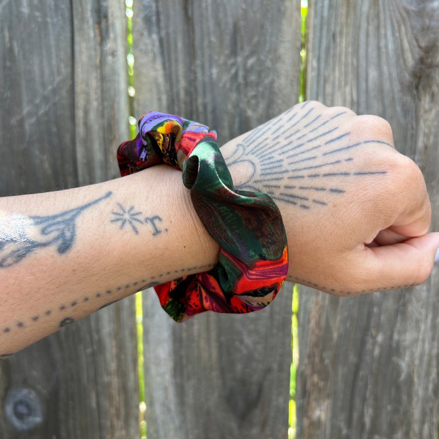 Hand wearing a colorful scrunchie with tattoos on a wooden surface