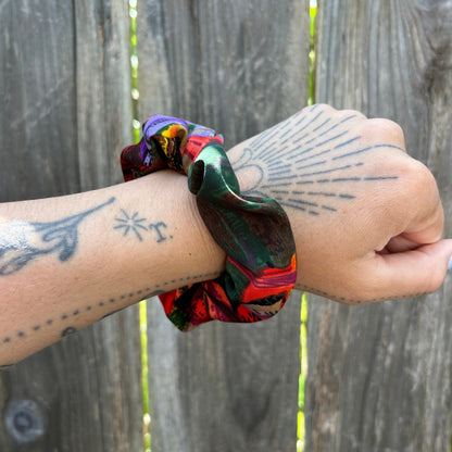 Hand wearing a colorful scrunchie with tattoos on a wooden surface