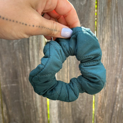 Teal scrunchie held by a hand against a wooden background
