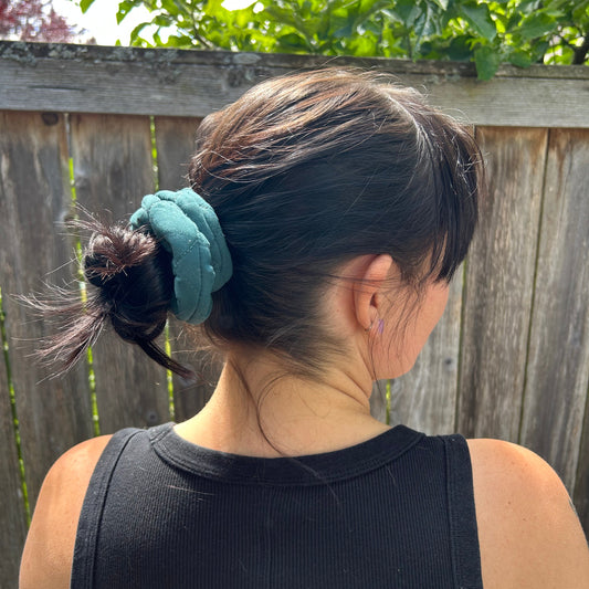 Person wearing a black tank top with a green scrunchie in their hair, standing outdoors.