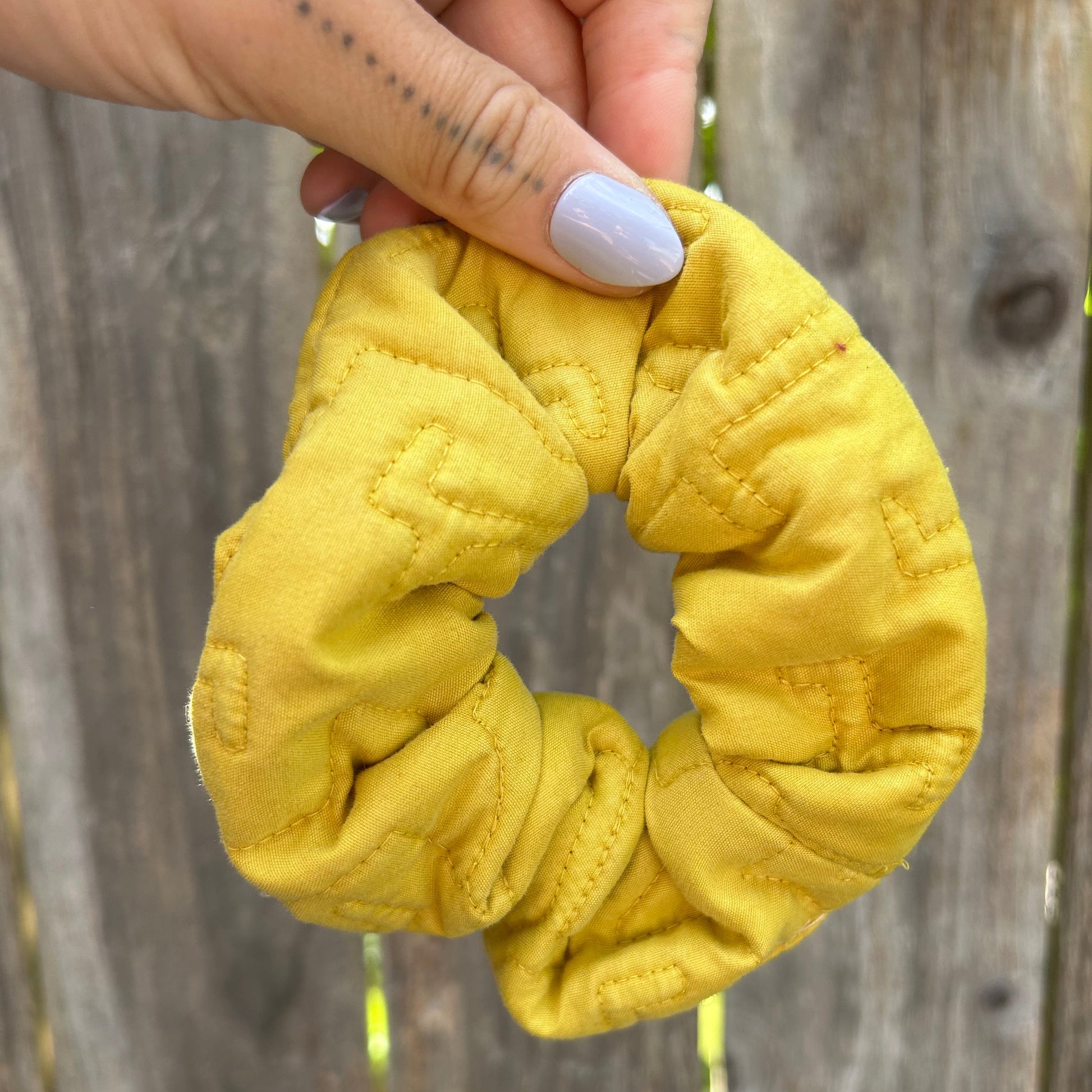 Yellow scrunchie held by a hand against a wooden background
