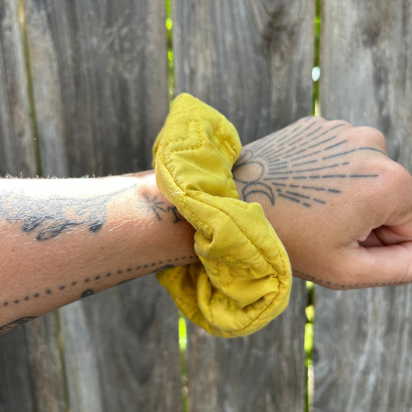Yellow scrunchie on a wrist with tattoos against a wooden background