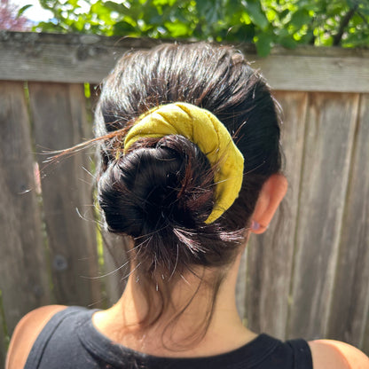 Person with a yellow scrunchie on their head, standing outdoors with greenery in the background