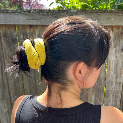 Person with a yellow hair tie in their hair, standing outdoors with greenery in the background.